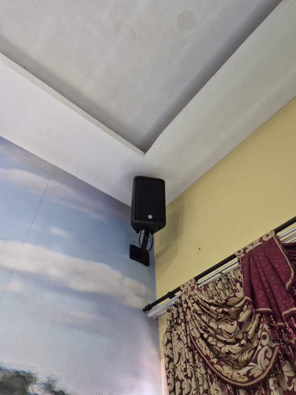 Loudspeaker mounted on a steel bracket high on the hall wall