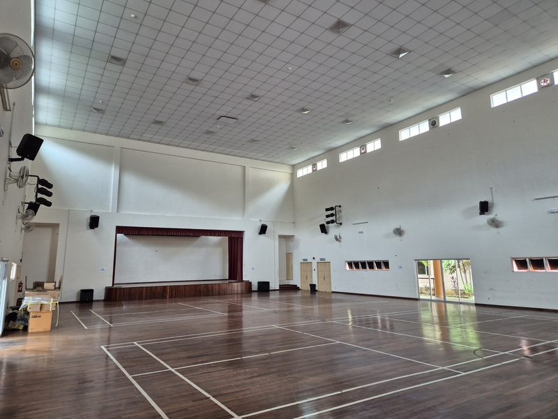 Wide view of the multipurpose hall showing the stage and loudspeakers distributed along both walls