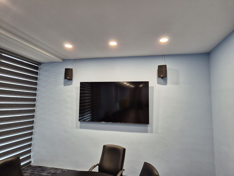 Boardroom with a wall-mounted display flanked by compact satellite loudspeakers