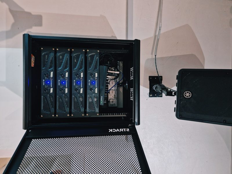 Yamaha loudspeaker on a wall bracket beside the wall-mounted rack of four amplifiers